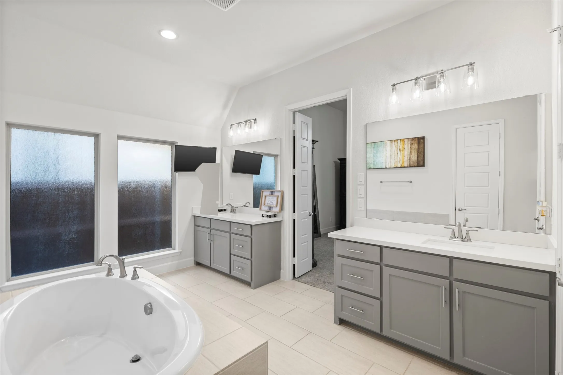 Spacious bathroom featuring a built-in soaking tub, dual vanity with undermount sinks, stone countertops, and tile flooring