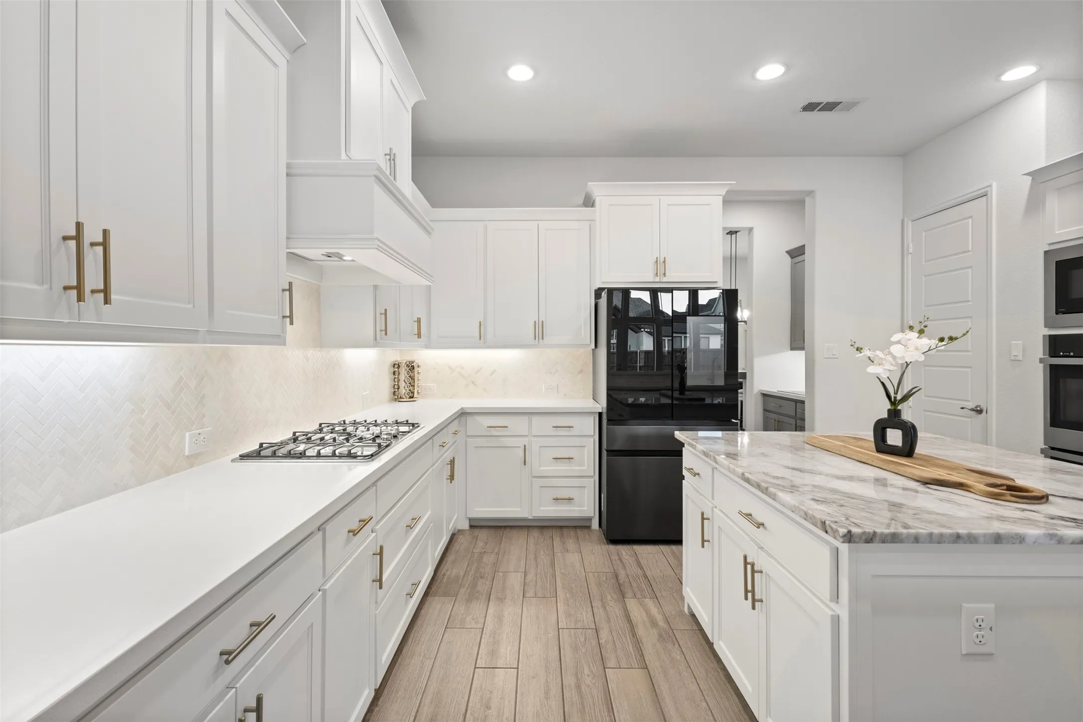 Modern kitchen featuring white cabinetry with gold-tone hardware, white countertops, and a herringbone-patterned tile backsplash