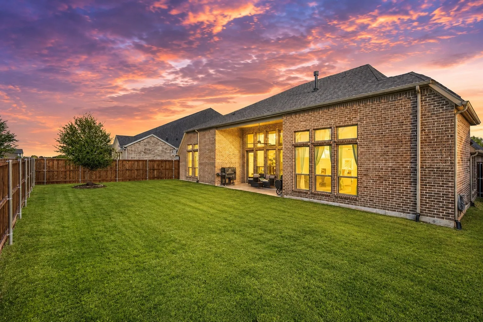 Expansive green lawn with a newly planted tree, surrounded by a wood privacy fence