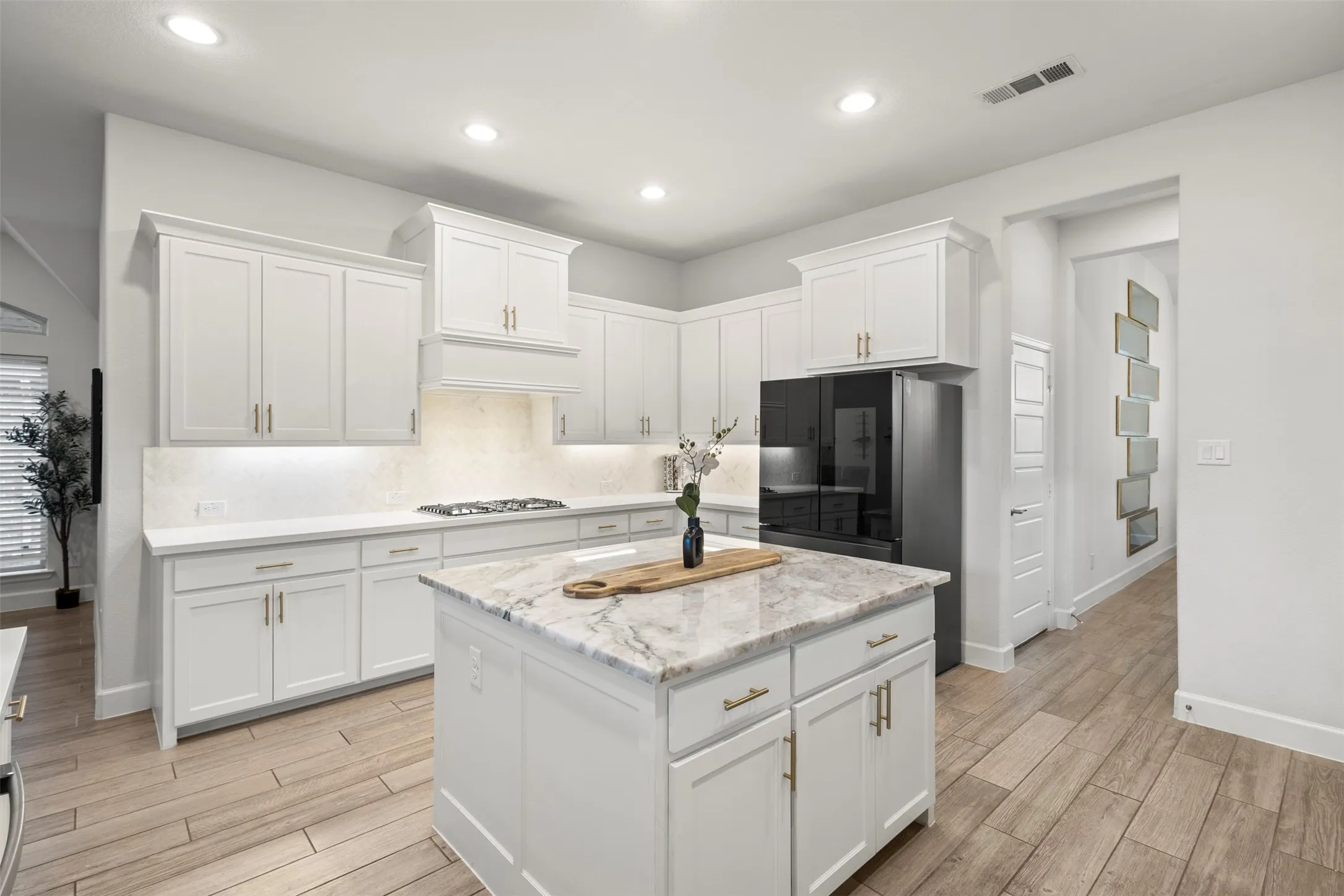 Kitchen featuring a central island with a light-toned countertop, white cabinetry with gold-finish hardware, recessed lighting, wood-finish flooring, and a stainless steel appliance
