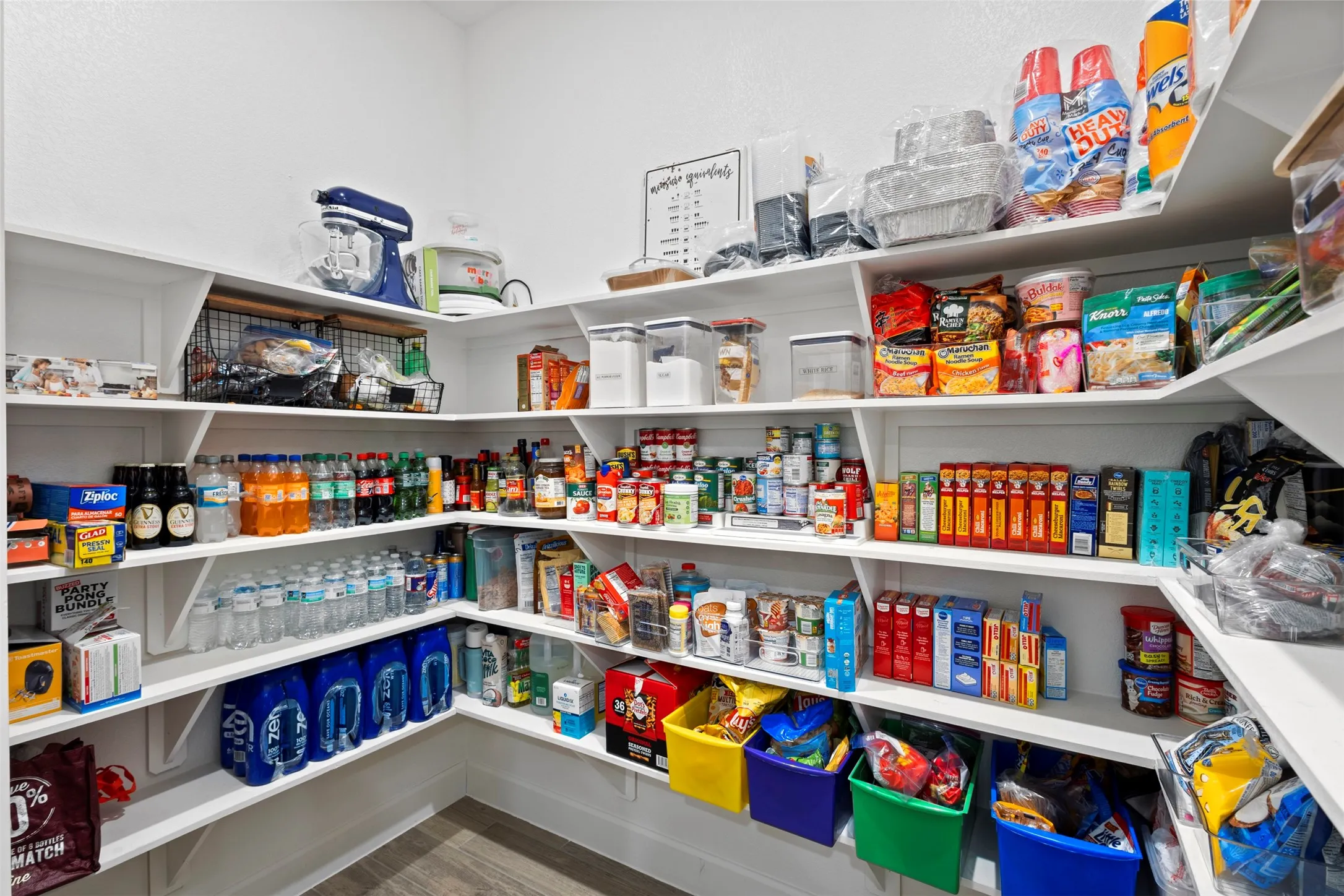 Spacious pantry featuring tiered shelving, L-shaped configuration, white-painted wood shelves, and wood-finish flooring