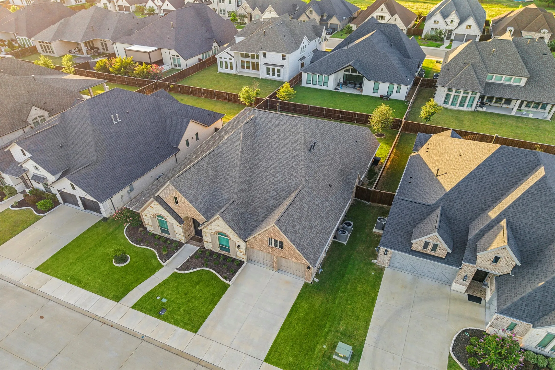 Aerial view showcasing a residential property featuring a brick and stone facade, a dark shingle roof, and a two-car garage