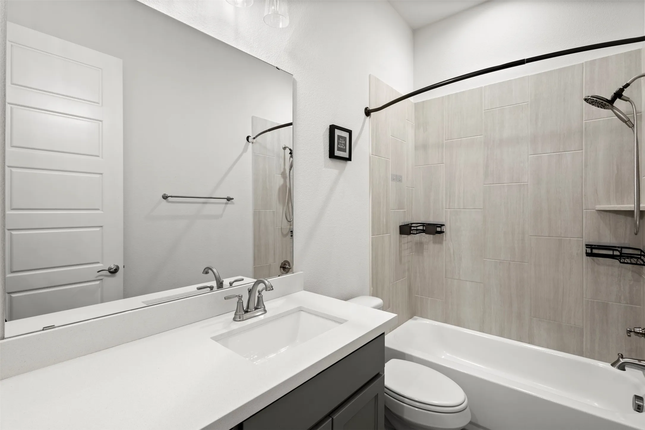 Bathroom featuring a white bathtub with a tiled surround, a contemporary vanity with a white countertop and integrated sink, and a large wall-mounted mirror