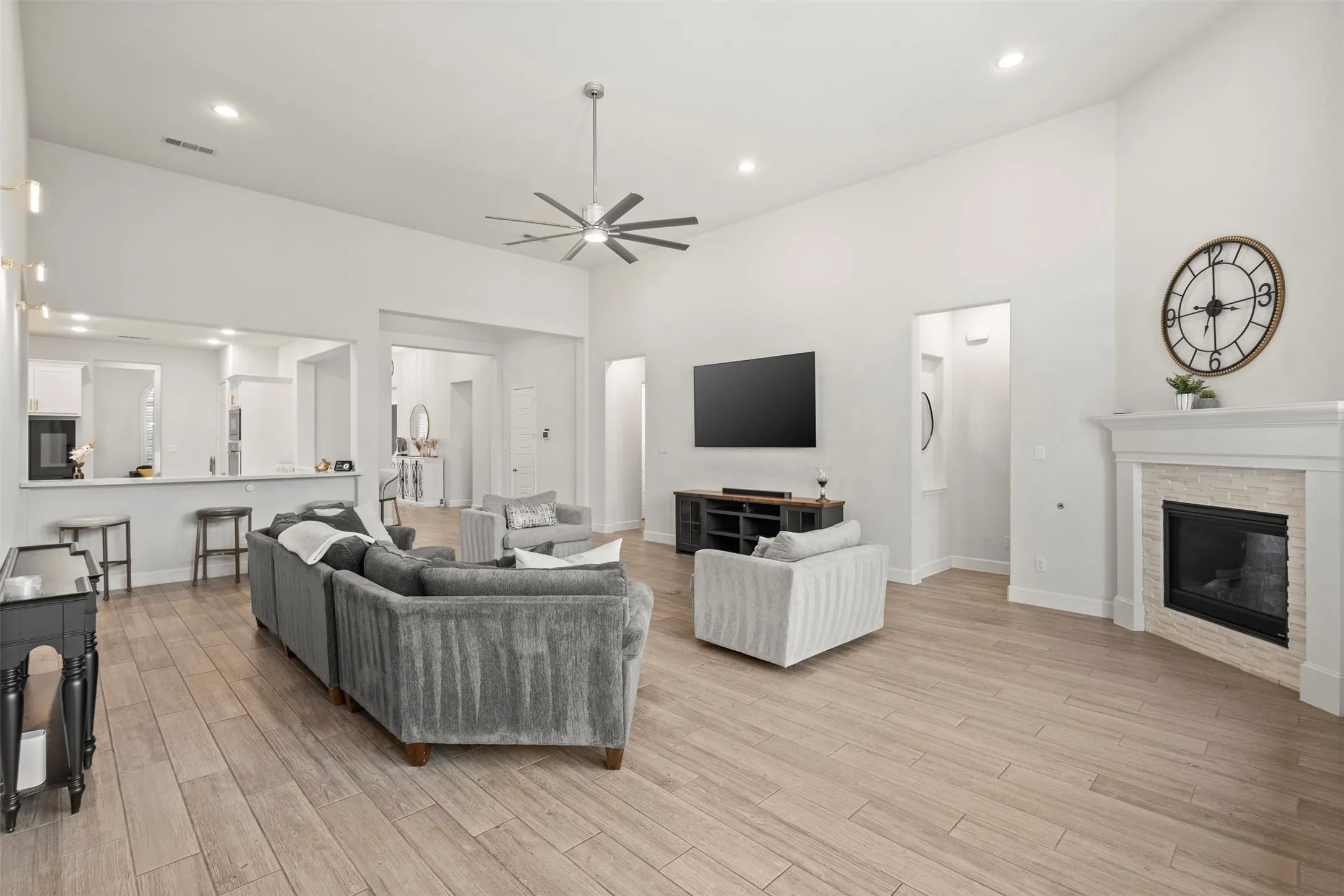 Spacious living area featuring high vaulted ceilings, wood-finish flooring, a contemporary ceiling fan, recessed lighting, and a fireplace with a stone surround and white mantel