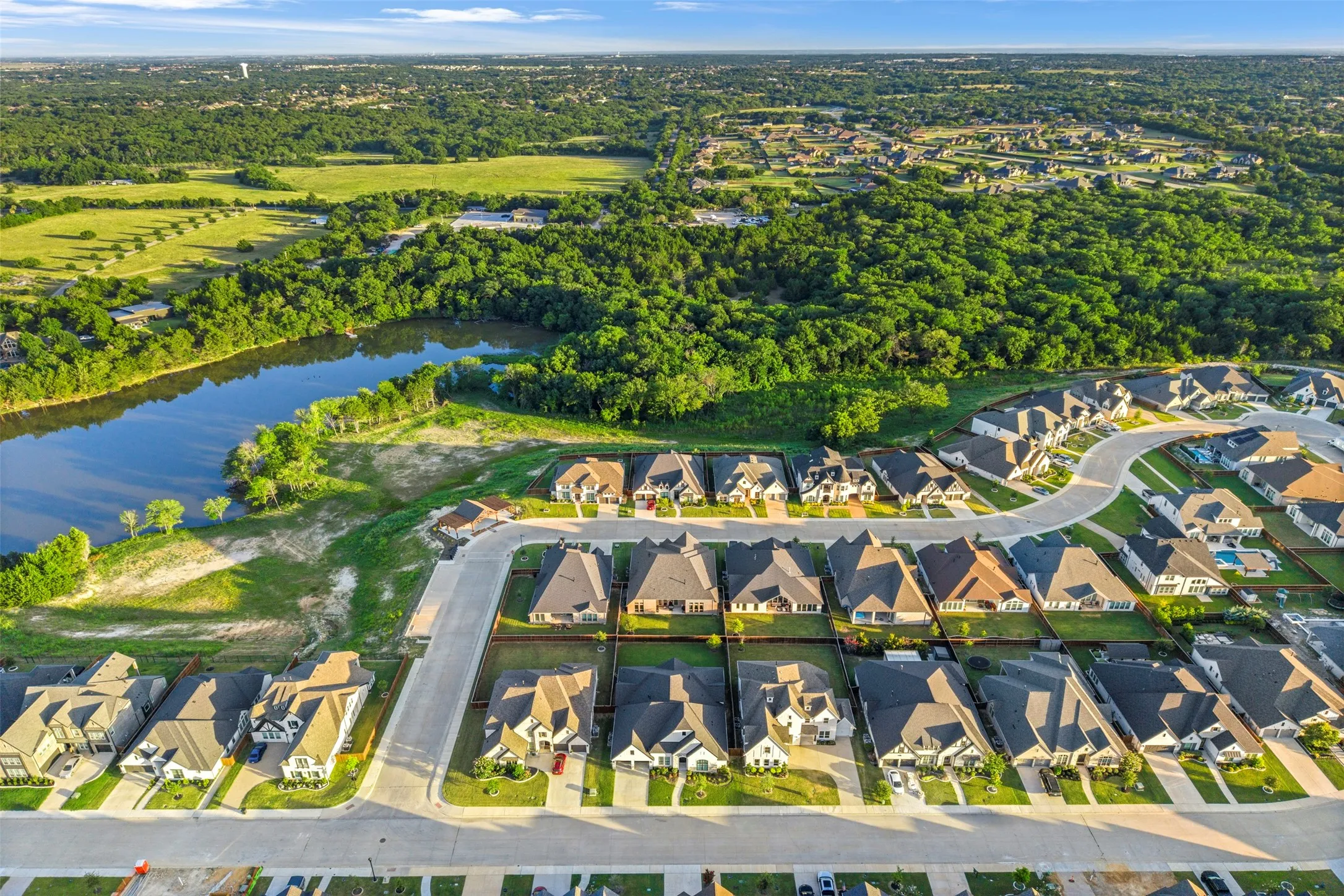 Aerial perspective showcasing a residential development with a curving street layout, surrounded by extensive green spaces and a prominent body of water