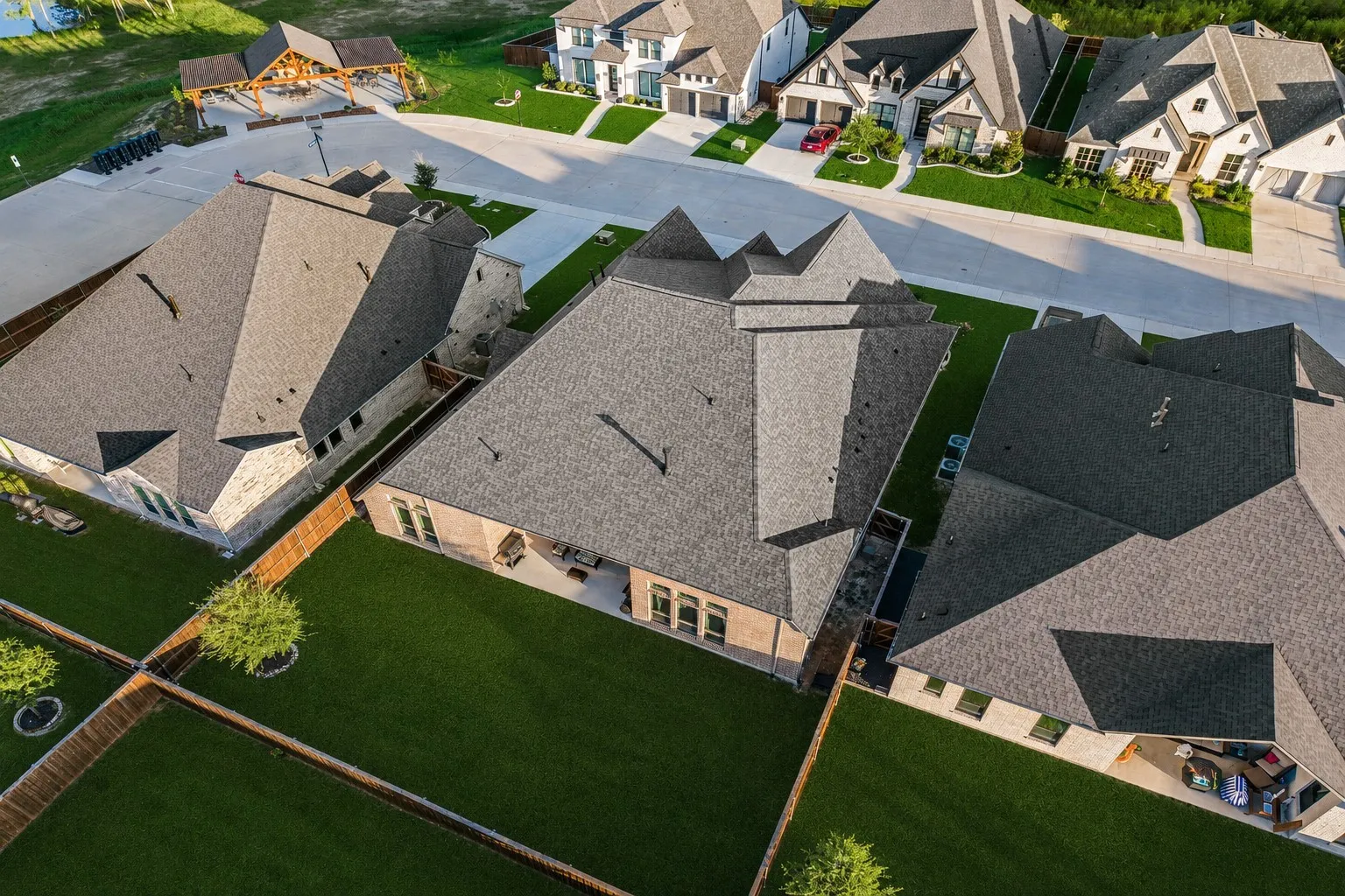 Aerial perspective showcasing a residential property featuring a multi-pitched shingle roof and a spacious, fenced backyard with manicured lawn