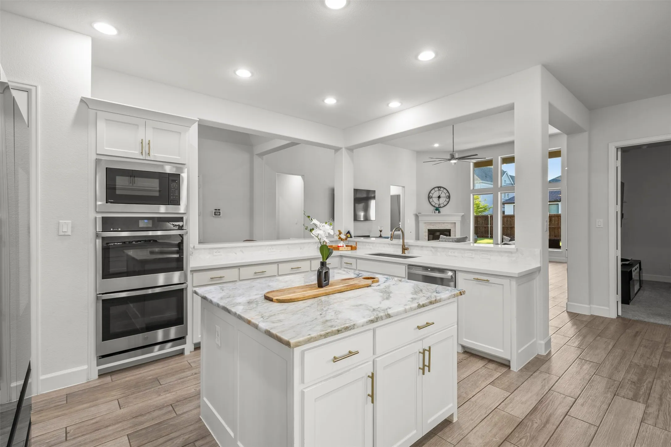 Kitchen featuring an eat-at island with a stone countertop, stainless steel appliances including a built-in microwave and double ovens, white cabinetry, and wood-finish flooring