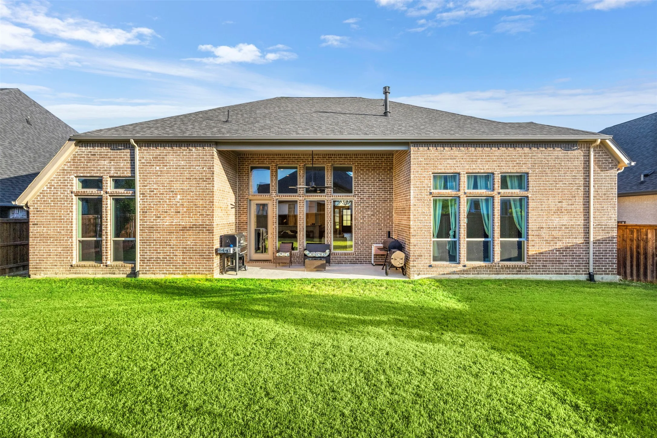 Brick exterior featuring a covered patio, expansive lawn, and multiple windows