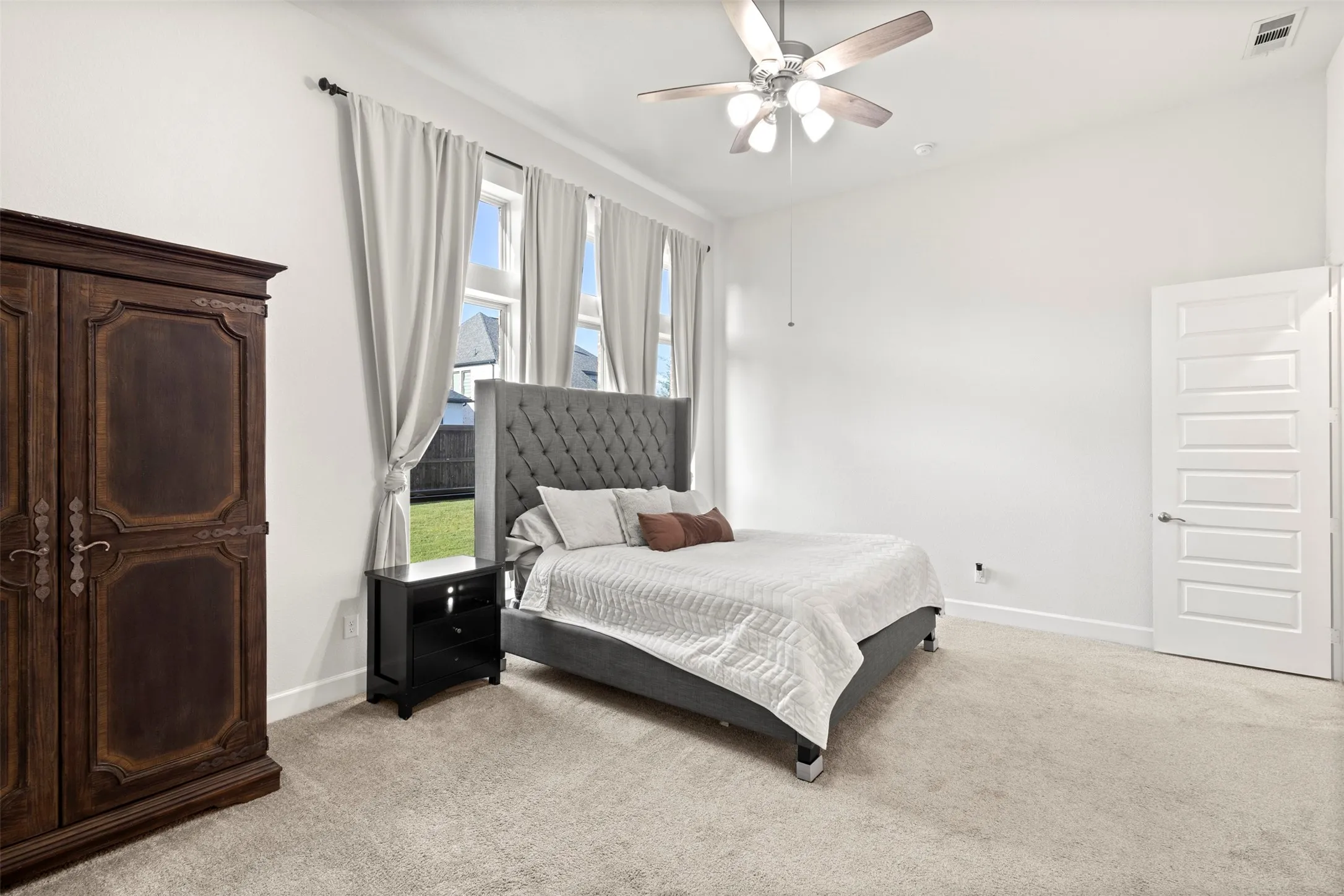 Spacious bedroom featuring light-colored carpeting, white baseboards, and a ceiling fan with integrated lighting