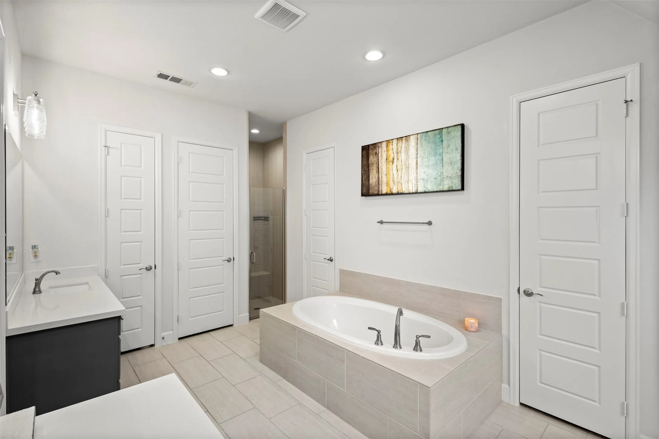 Soaking tub featuring a tiled surround, dual-sink vanity with quartz countertop, walk-in shower with glass enclosure, recessed lighting, and large format tile flooring
