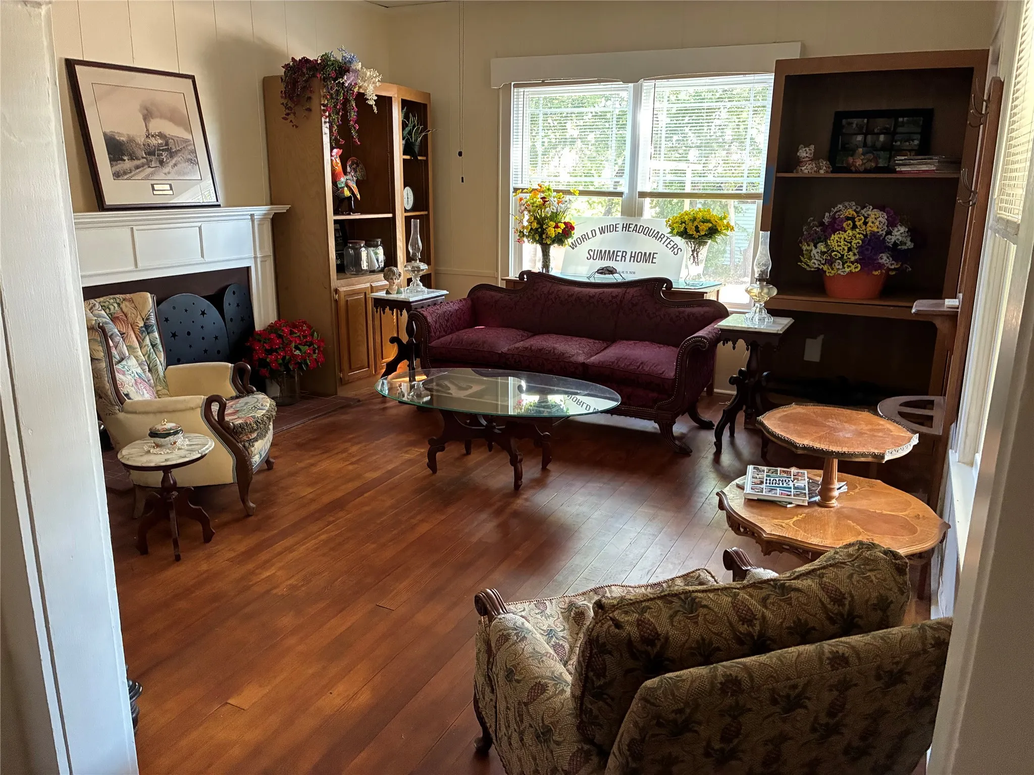 Warm wood-finish flooring, white paneled walls, and a classic fireplace with a white mantel