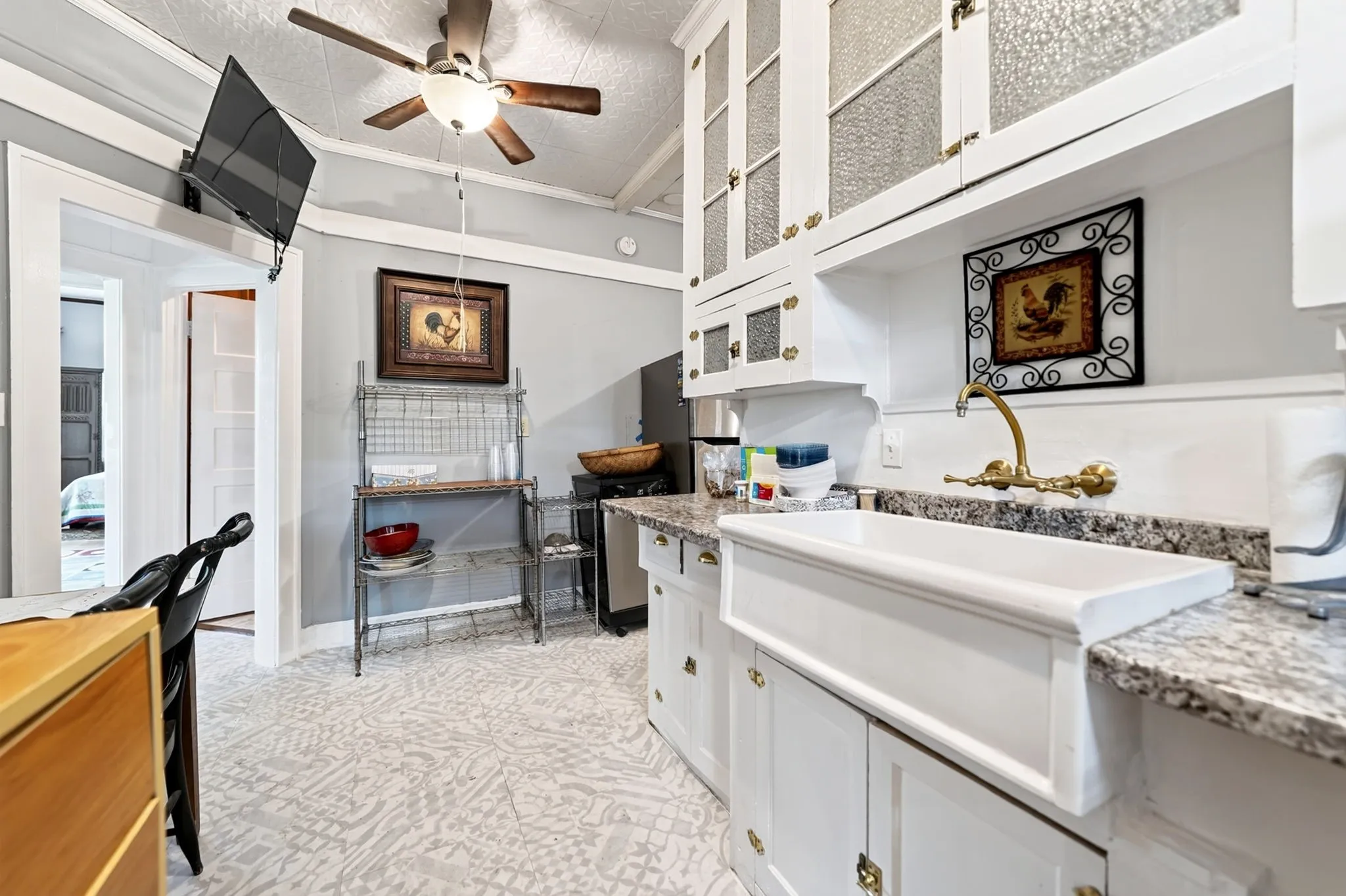 Kitchen featuring a white farmhouse sink, granite-finish countertops, white cabinetry with brass-tone hardware, and an exposed wall-mounted faucet