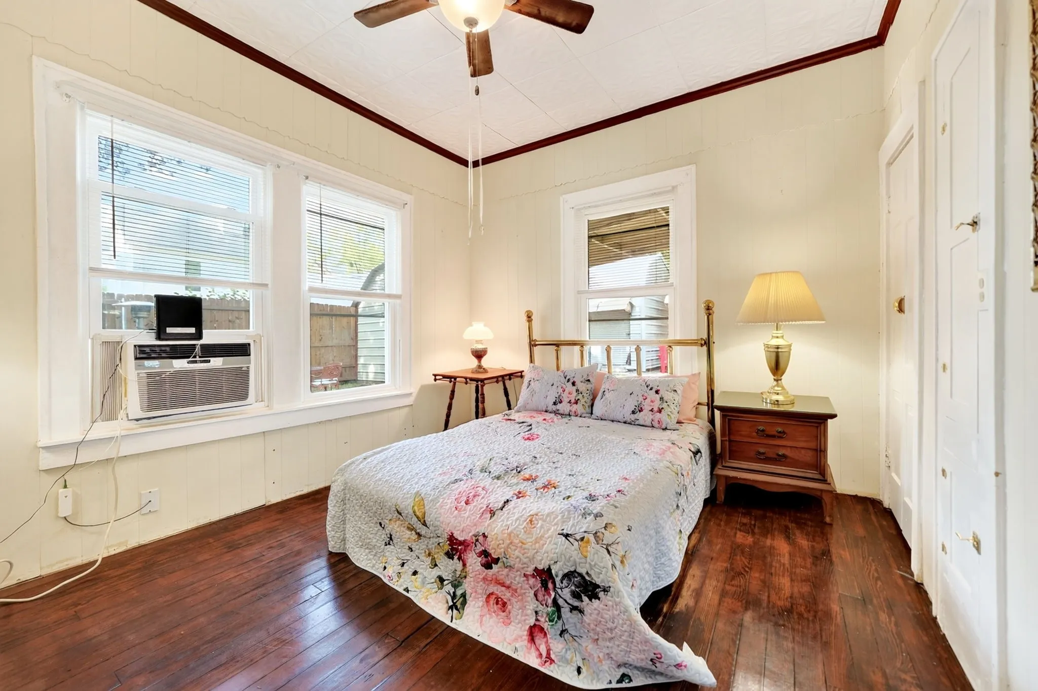 Interior room featuring wood-finish flooring, two large windows with blinds, a ceiling fan, and white paneled doors