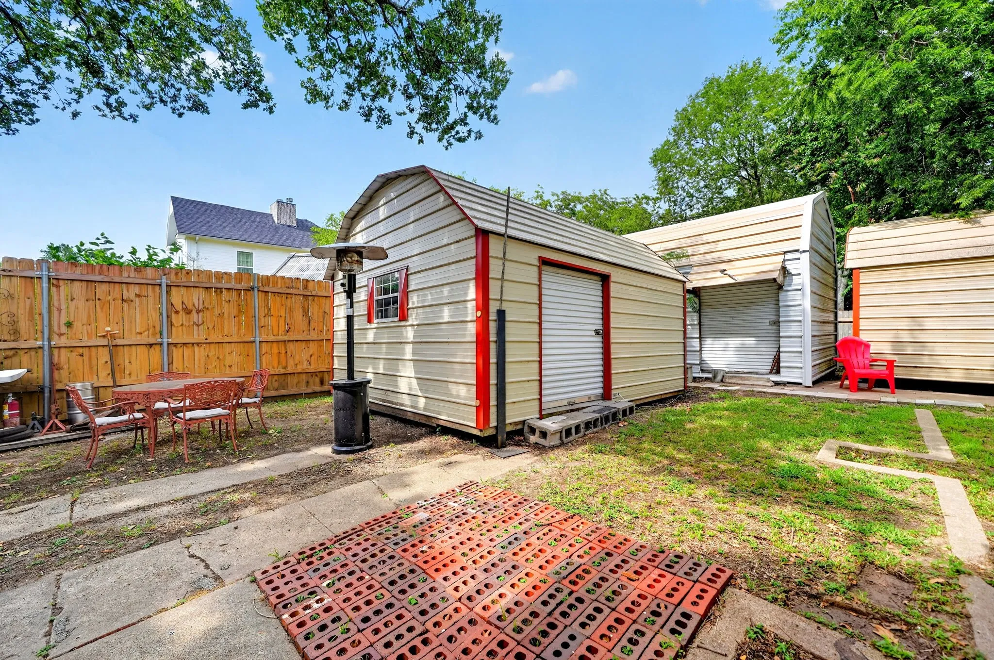 Backyard featuring three storage sheds with metal siding and roll-up doors, a wood privacy fence, and a concrete patio area