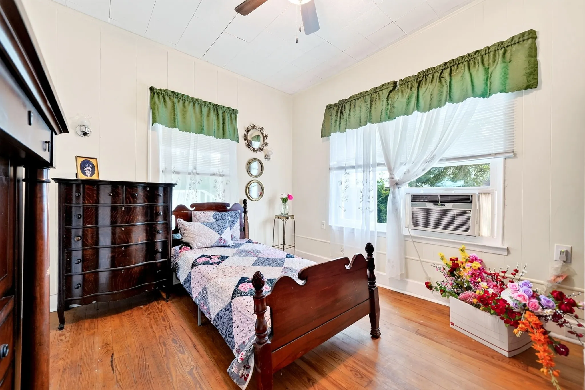 Bedroom featuring wood-finish flooring, white paneled walls, and a ceiling fan