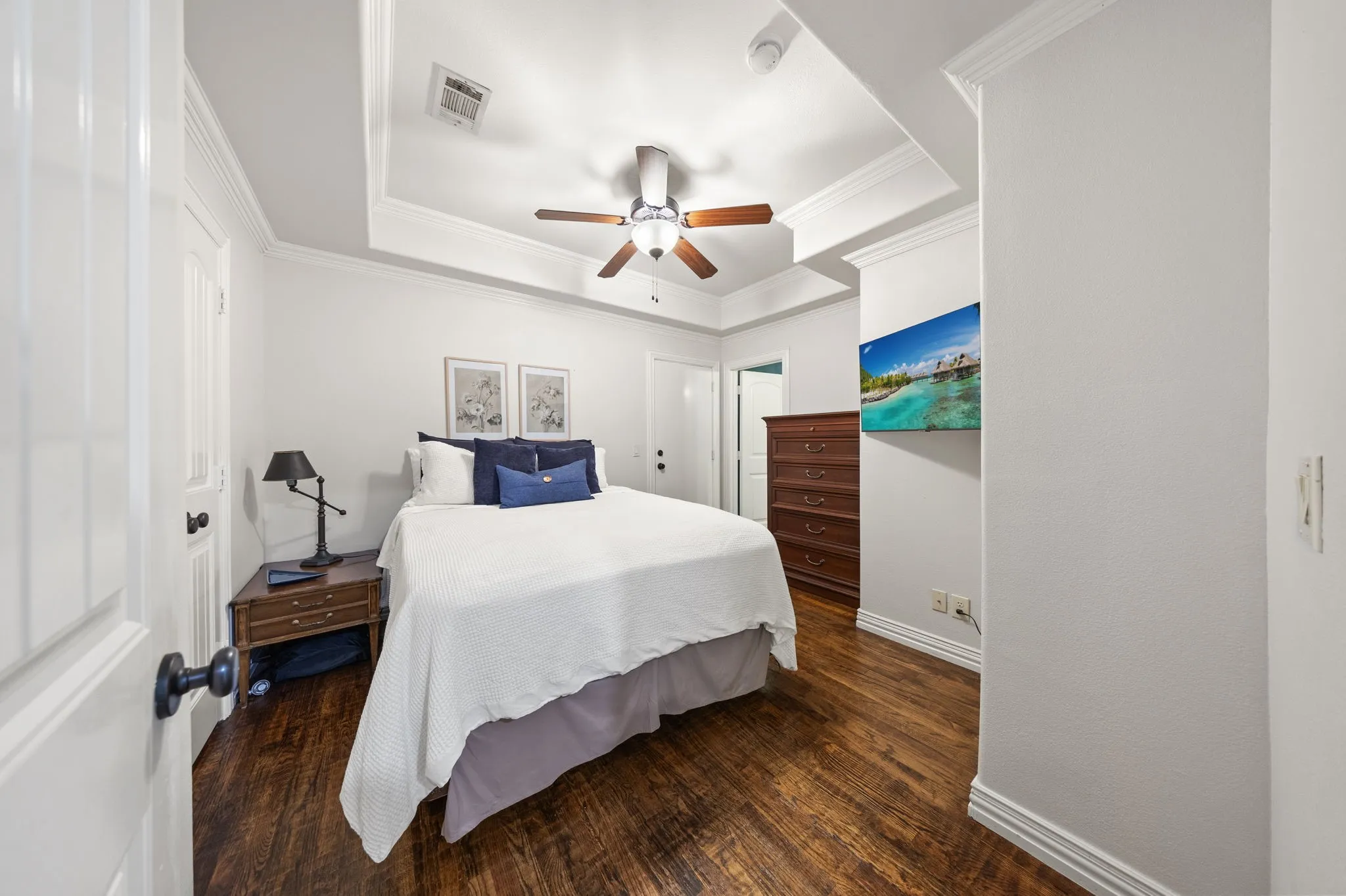 Bedroom featuring wood-finish flooring, a tray ceiling with crown molding, and a ceiling fan