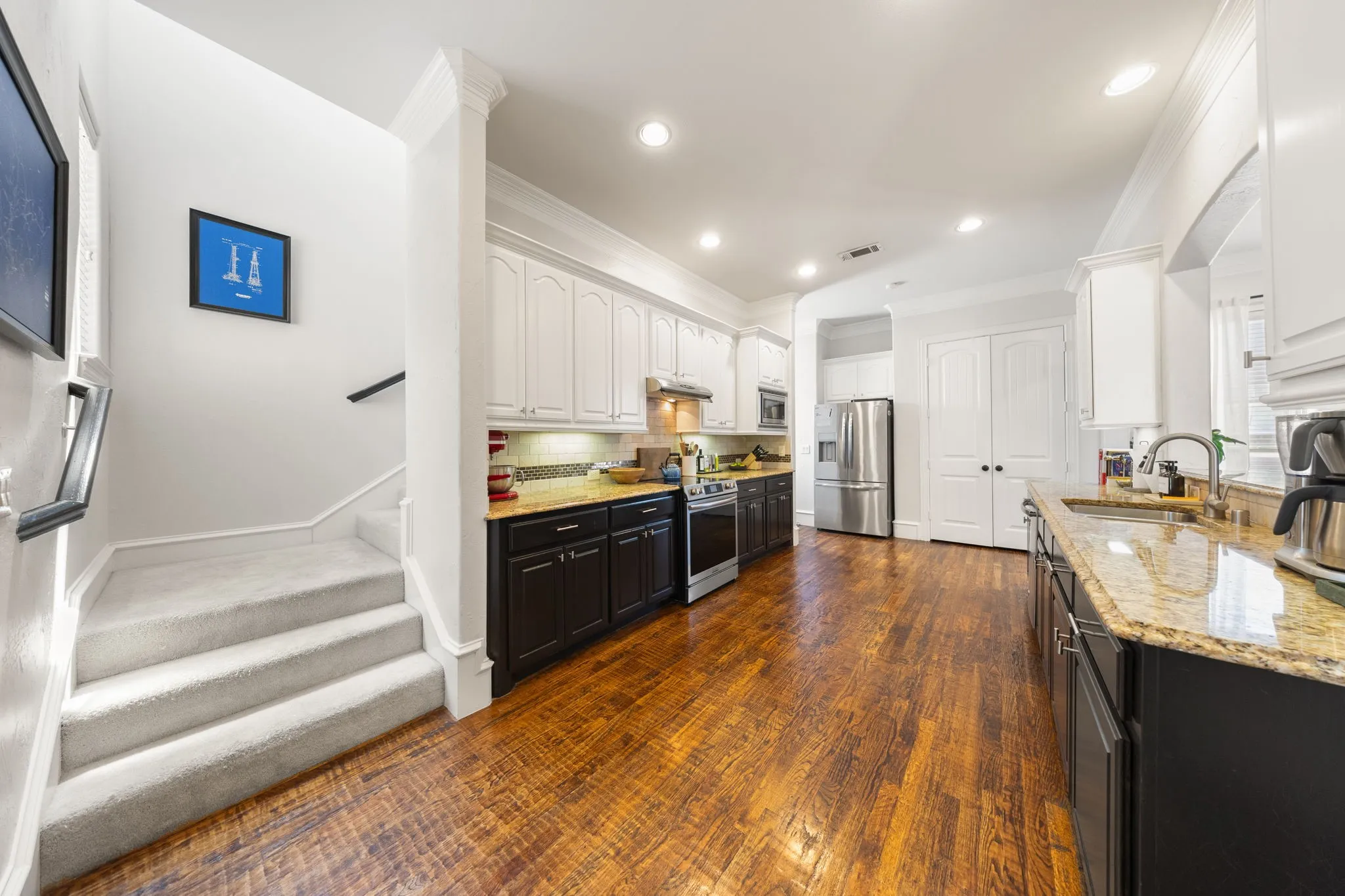 Expansive kitchen featuring wood-finish flooring, two-tone cabinetry, stainless steel appliances, granite countertops, and recessed lighting