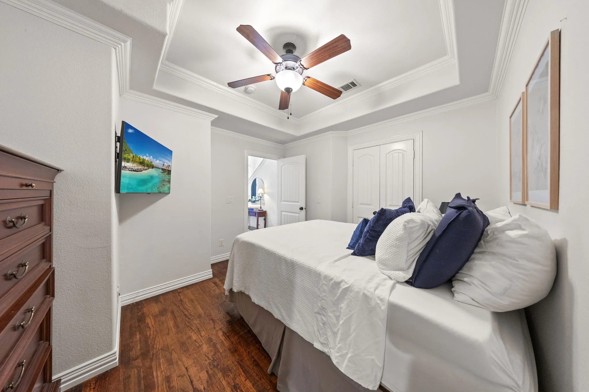 Tray ceiling with decorative molding, wood-finish flooring, and a ceiling fan with light fixture