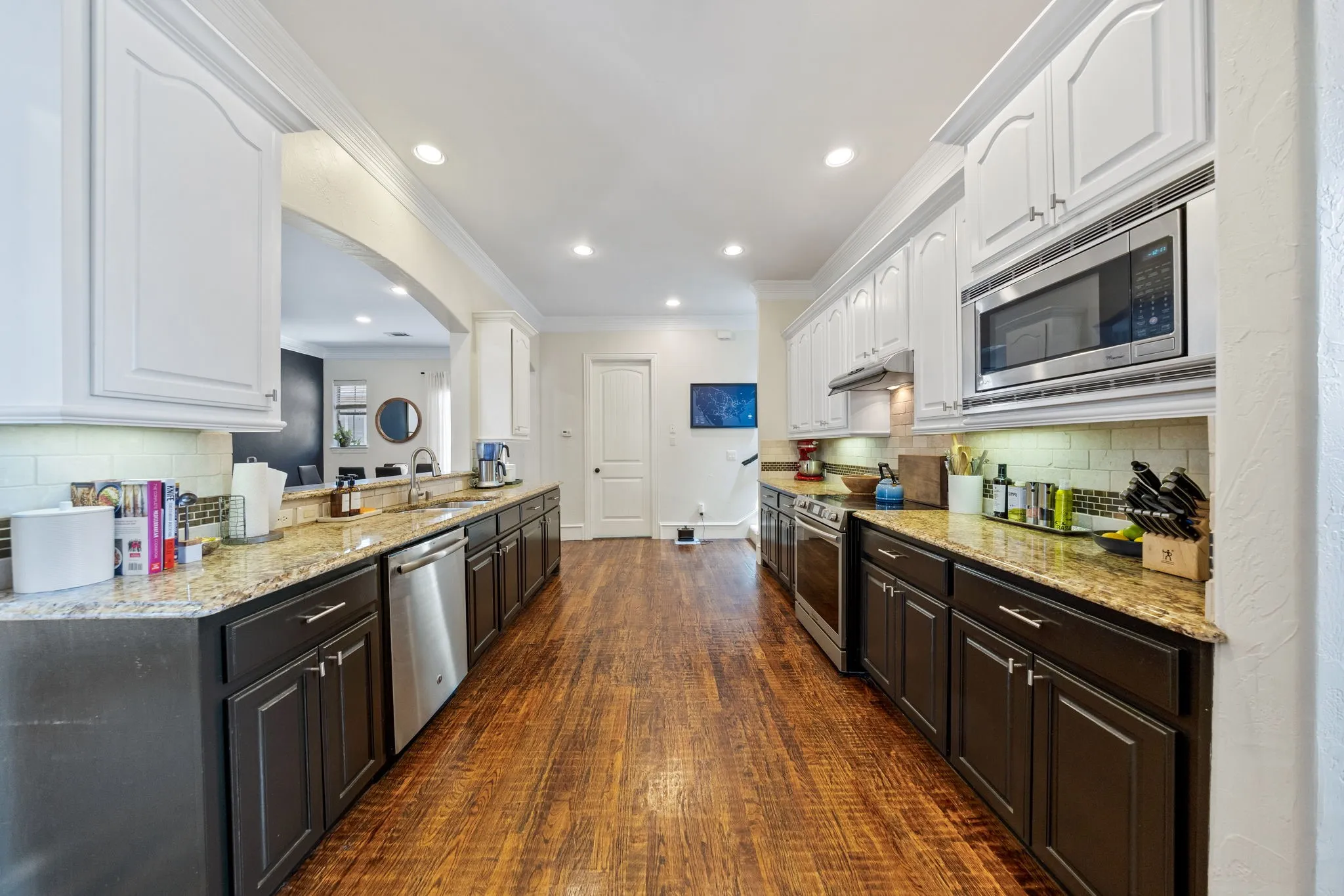 Galley kitchen featuring wood-finish flooring, two-tone cabinetry with white upper and dark lower units, granite countertops, and stainless steel appliances