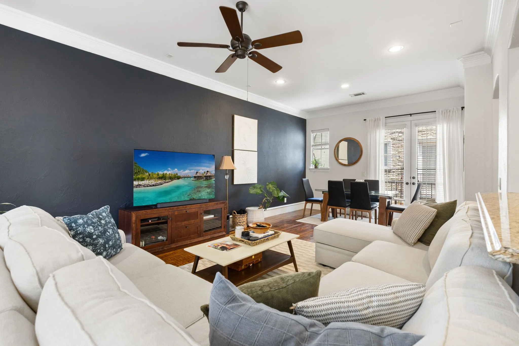 Open-concept living area with dark accent wall, crown molding, and wood-finish flooring