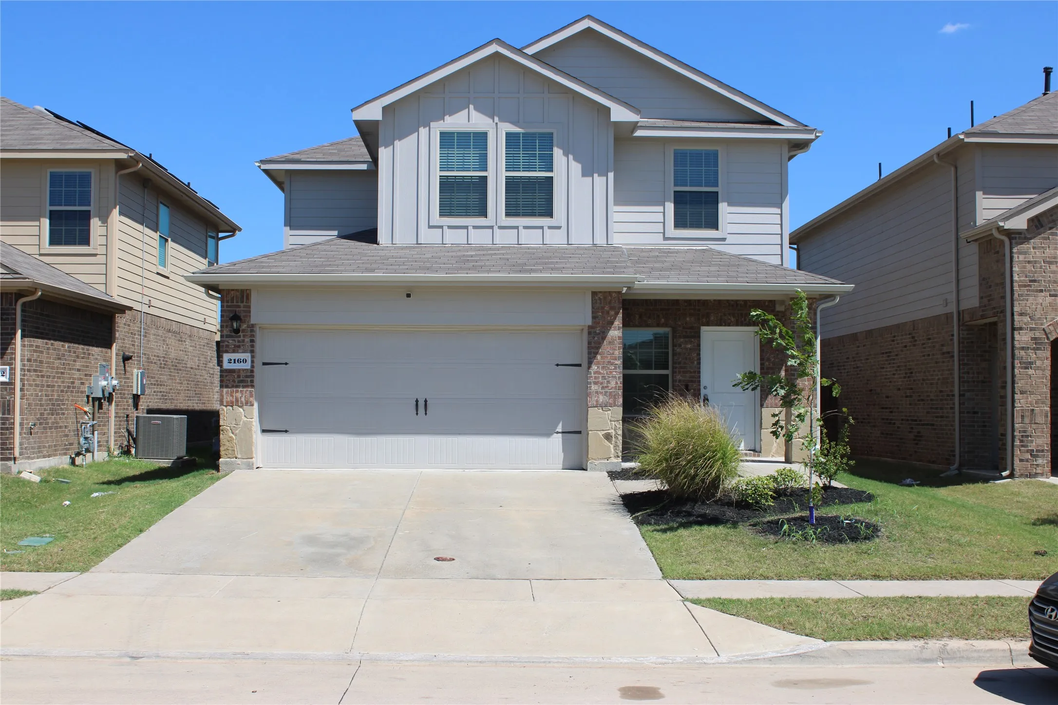 Two-story residence featuring a two-car garage, brick and siding exterior, front porch entry, and a concrete driveway