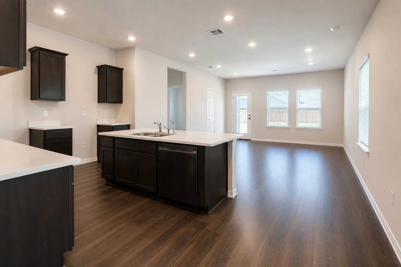 Open-concept kitchen and living area featuring dark wood-finish flooring, recessed lighting, and crisp white walls