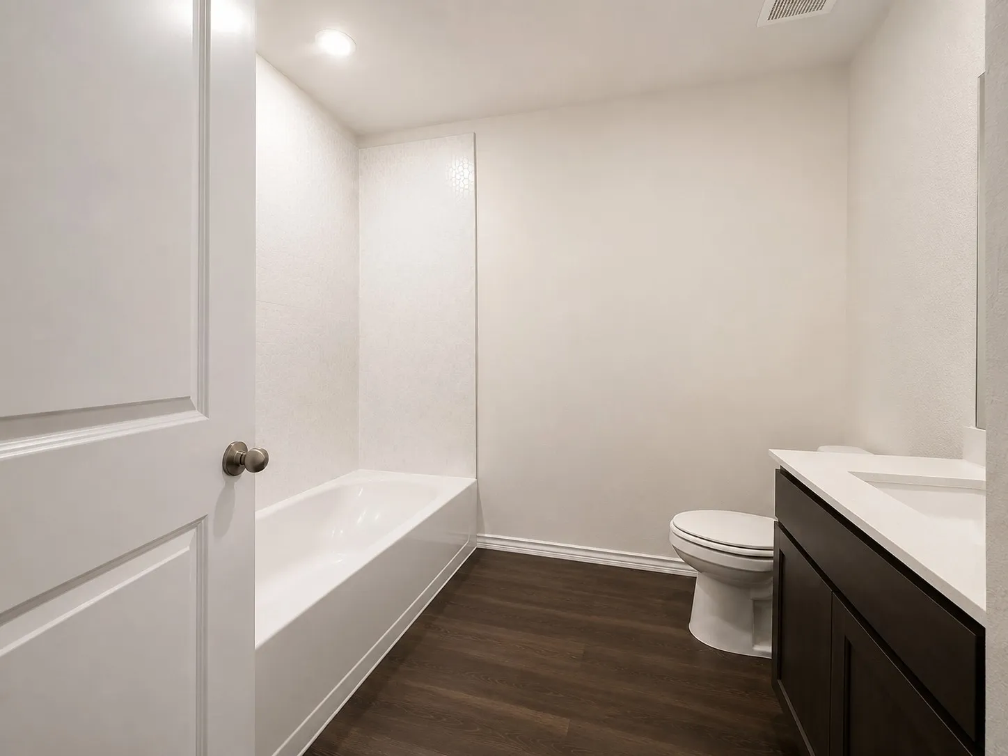 Full bathroom featuring a tub-shower combination with patterned tile surround, a dark wood-finish vanity with a white countertop and integrated sink, and wood-finish flooring