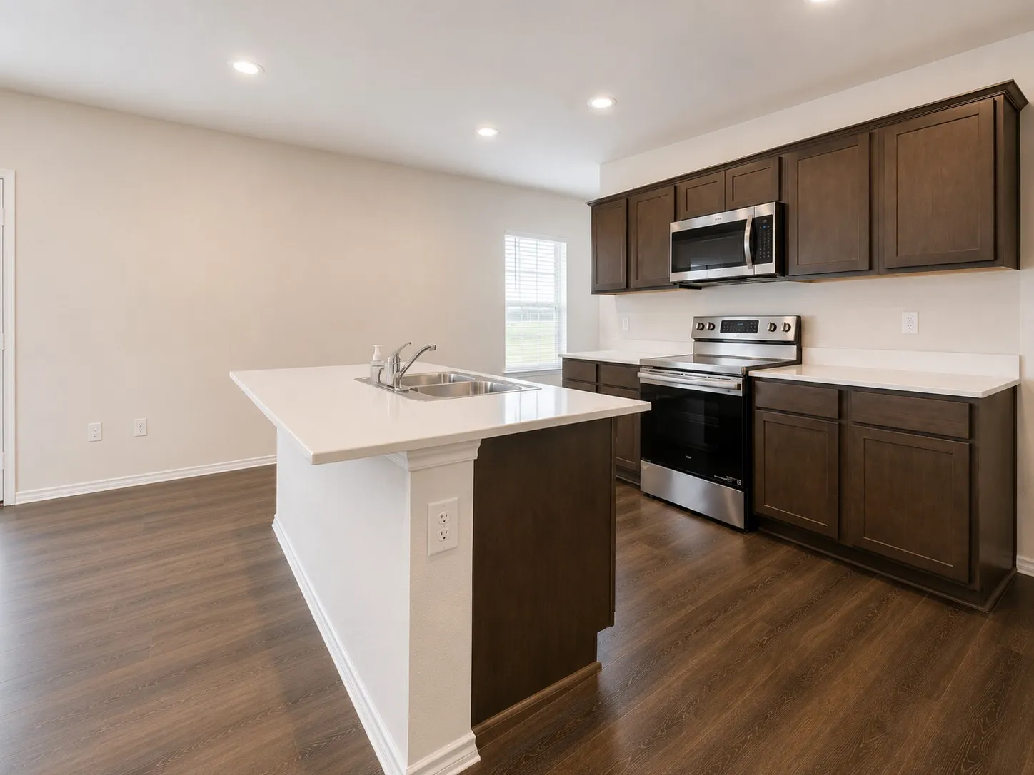 Kitchen featuring a central island with an undermount sink, dark wood-finish cabinetry, stainless steel appliances, and wood-finish flooring