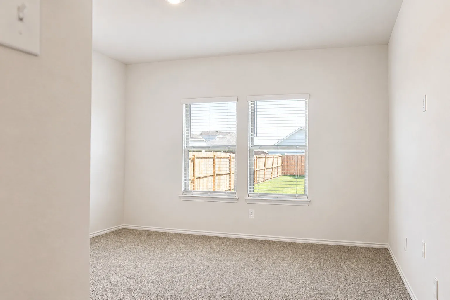 Spacious interior room with neutral-toned walls, plush grey carpeting, and white trim