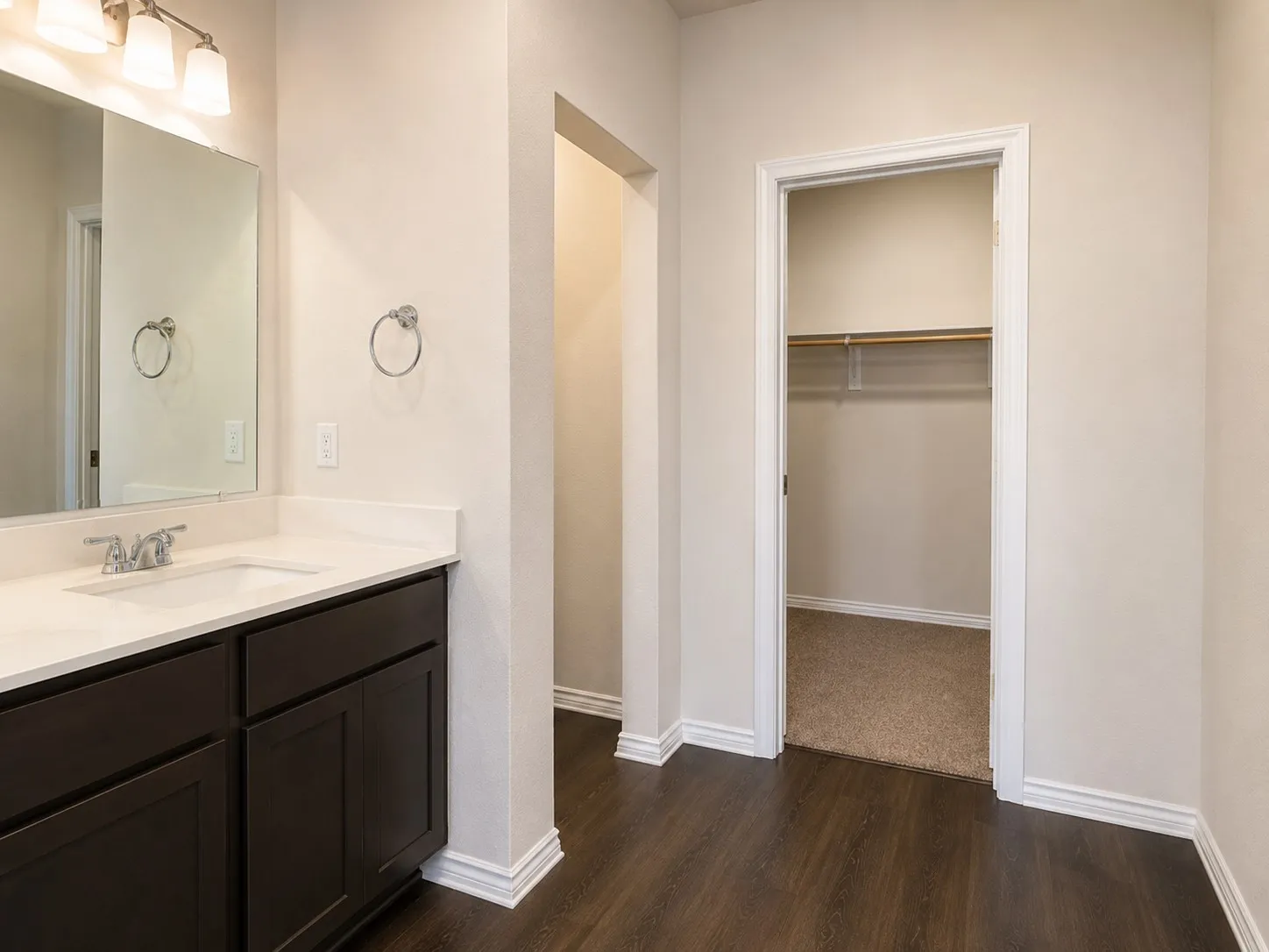 Bathroom vanity featuring a white countertop with integrated sink, dark wood-finish cabinetry, and a chrome faucet