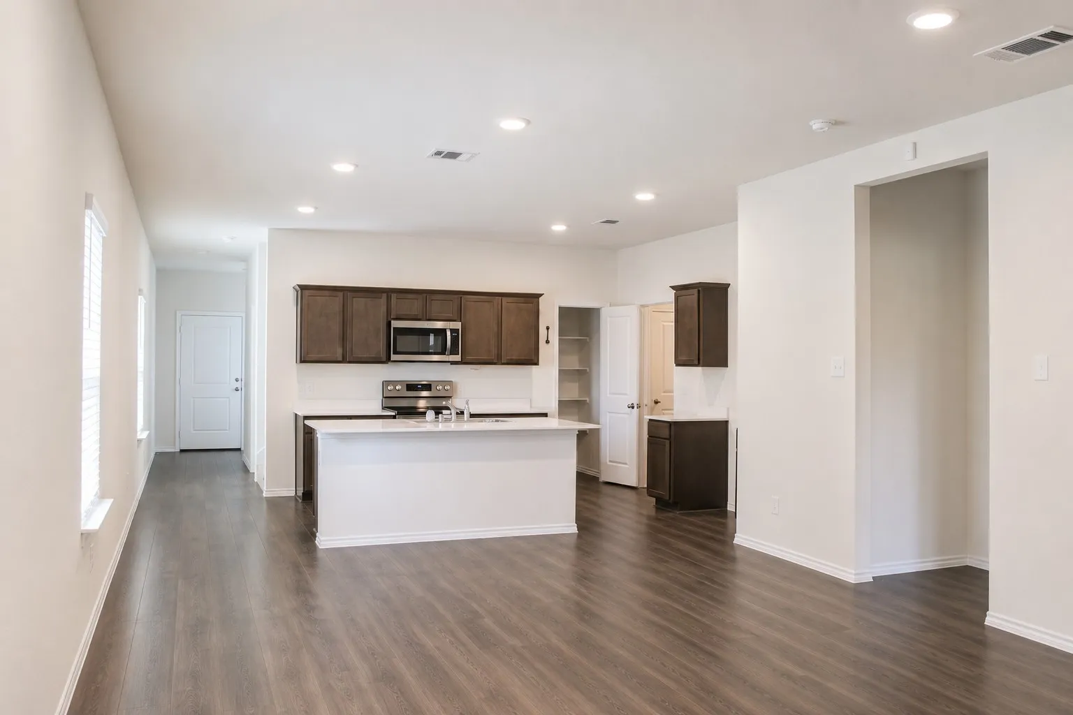 Open-concept living space featuring wood-finish flooring, recessed lighting, and a kitchen island with white countertops