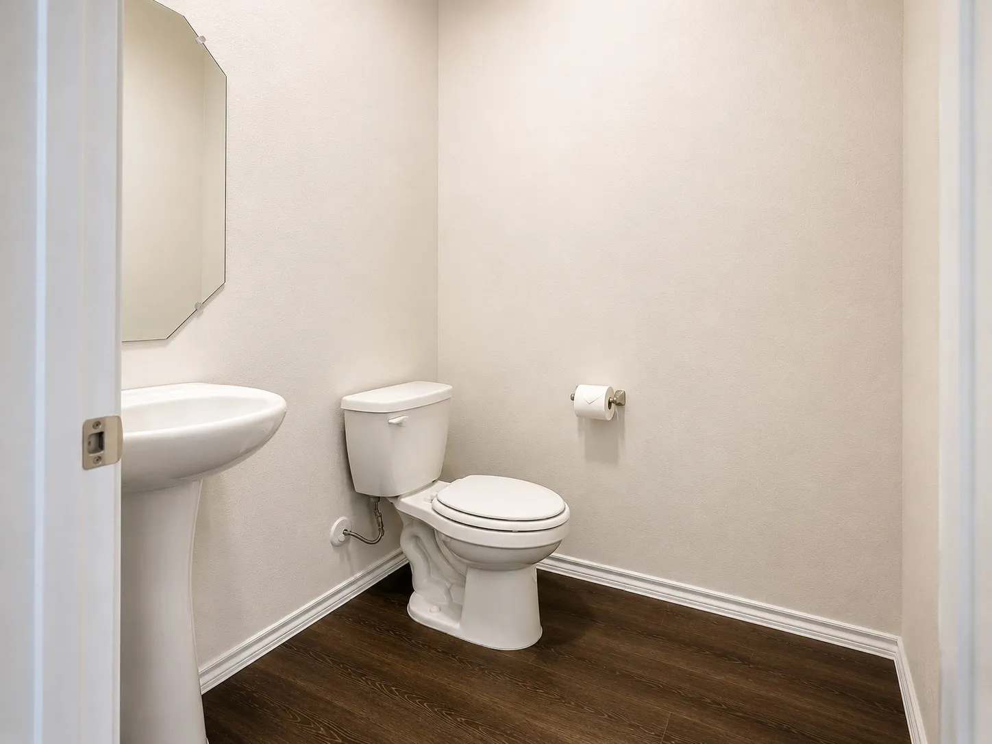 Bathroom featuring a pedestal sink, a toilet, wood-finish flooring, and a decorative wall mirror
