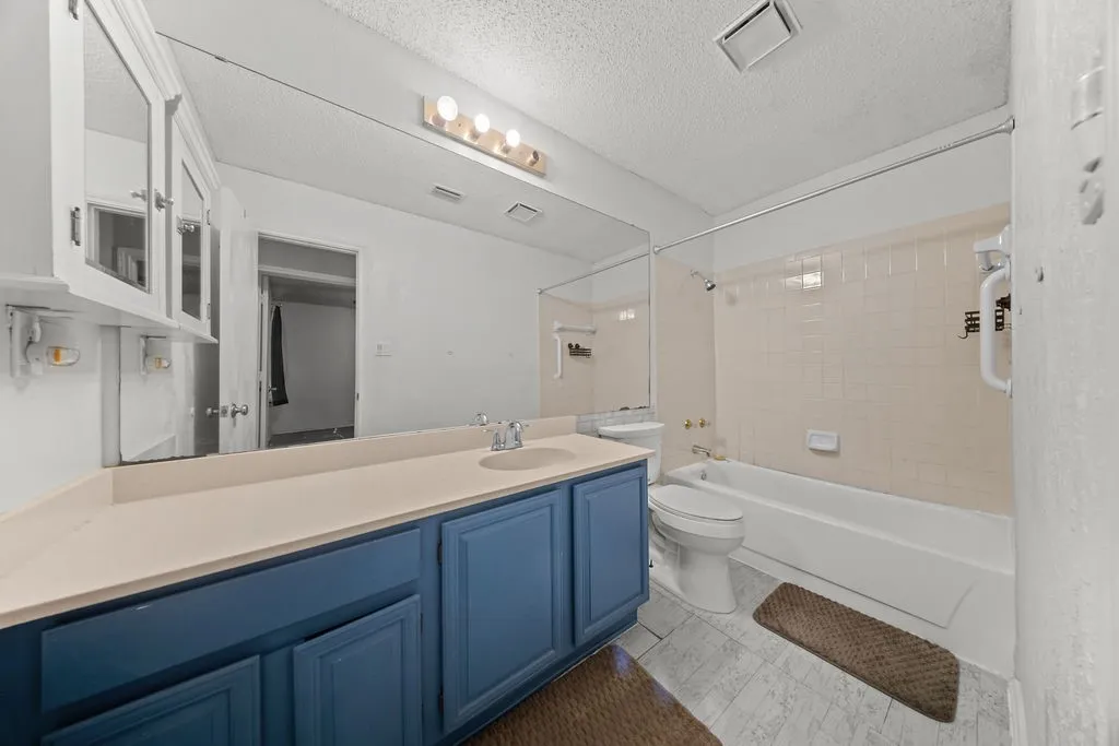 Bathroom featuring a vanity with blue base cabinetry and a light-toned countertop, a full wall mirror, and a shower-tub combination with light-colored subway tile surround