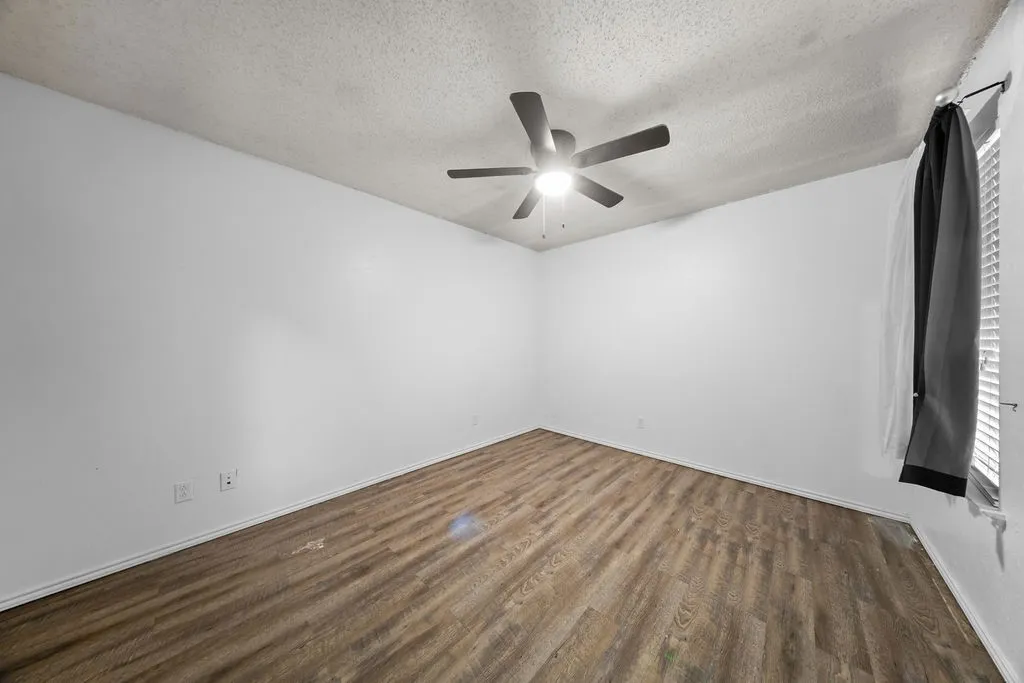 Bright room featuring wood-finish flooring, a ceiling fan with integrated lighting, and white baseboards