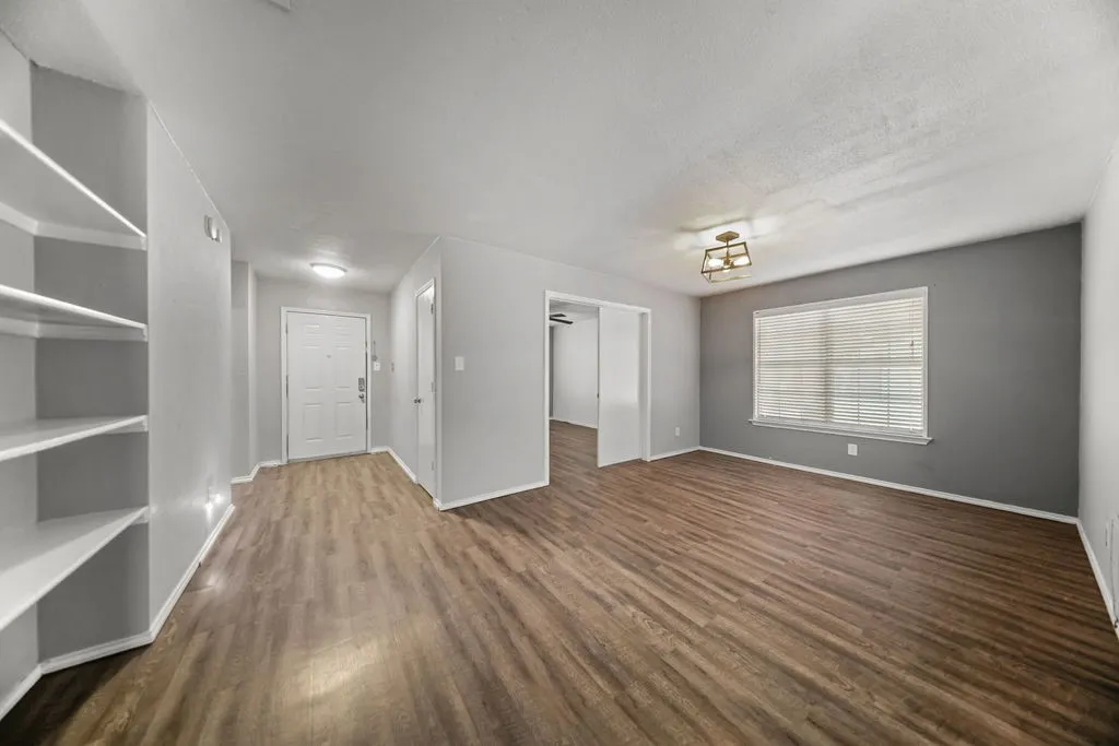 Open concept living area with wood-finish flooring, built-in shelving, a front entry door, and a window with blinds
