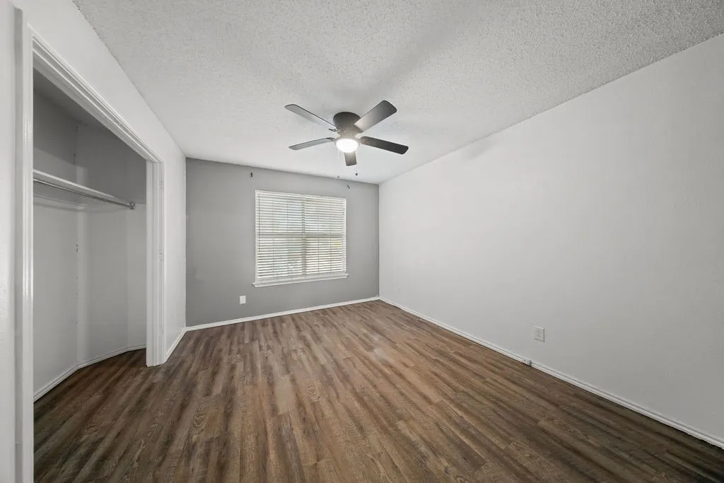 Spacious room featuring wood-finish flooring, a ceiling fan with integrated lighting, and a window with blinds