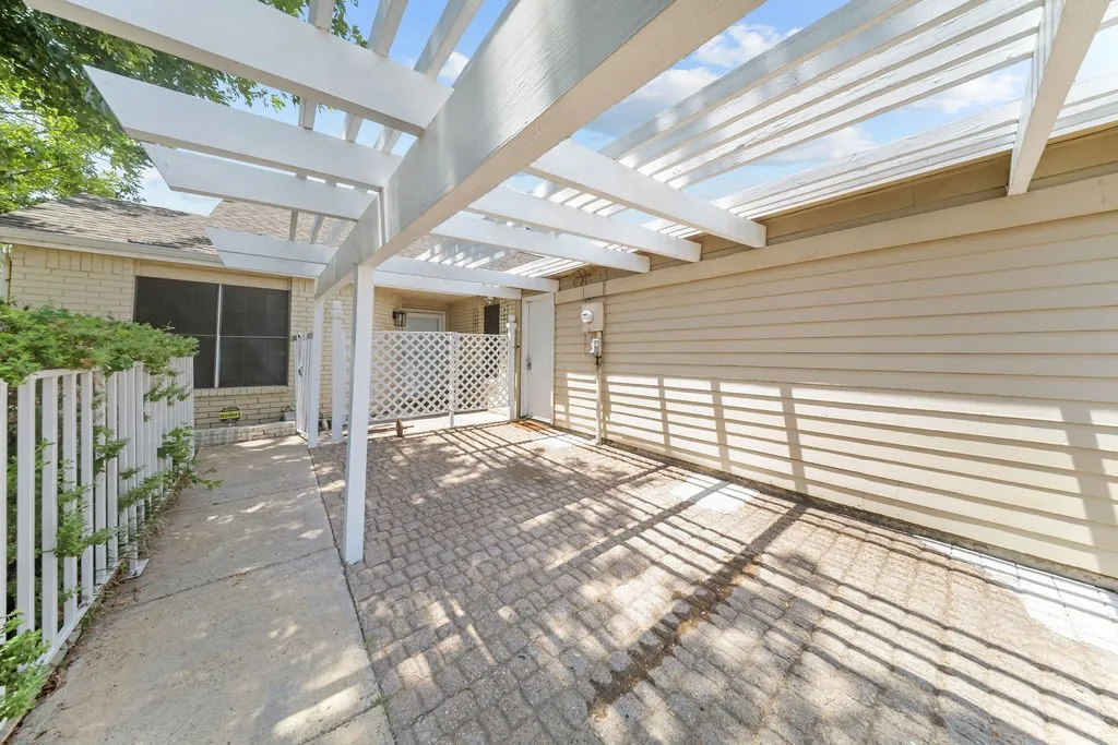 Covered patio featuring a white pergola structure, paver flooring, and vertical lattice privacy screening