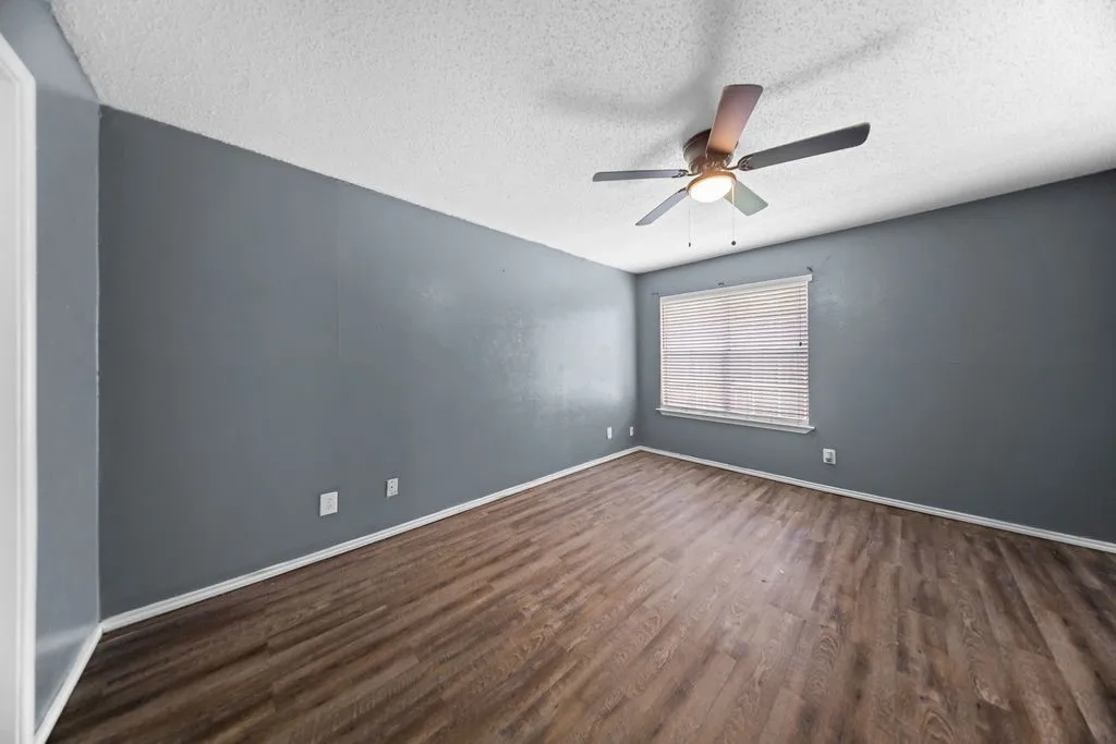 Spacious room featuring wood-finish flooring, a ceiling fan with integrated lighting, and a window with horizontal blinds