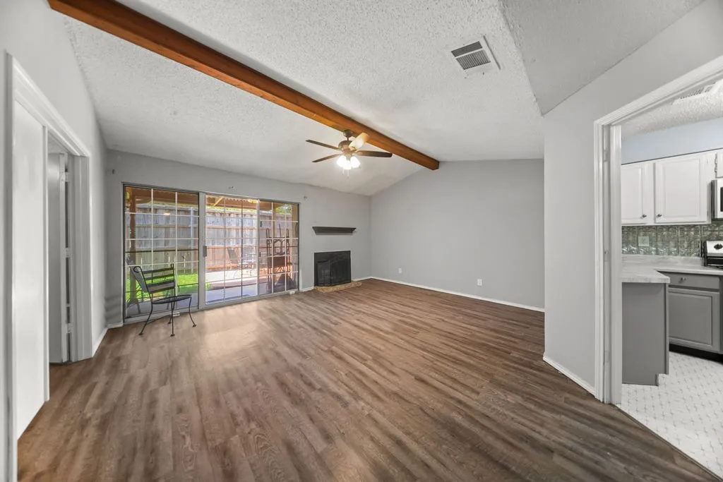 Open concept living area featuring wood-finish flooring, a vaulted ceiling with a prominent wood beam, and a ceiling fan