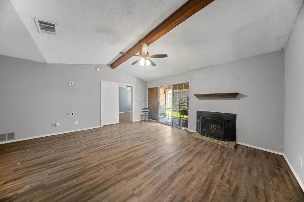 Spacious room featuring wood-finish flooring, a vaulted ceiling with exposed wood beams, and a ceiling fan