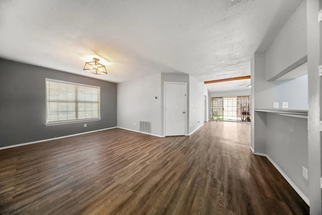 Spacious room featuring wood-finish flooring, a contemporary ceiling light fixture, a large window with blinds, and a built-in shelf