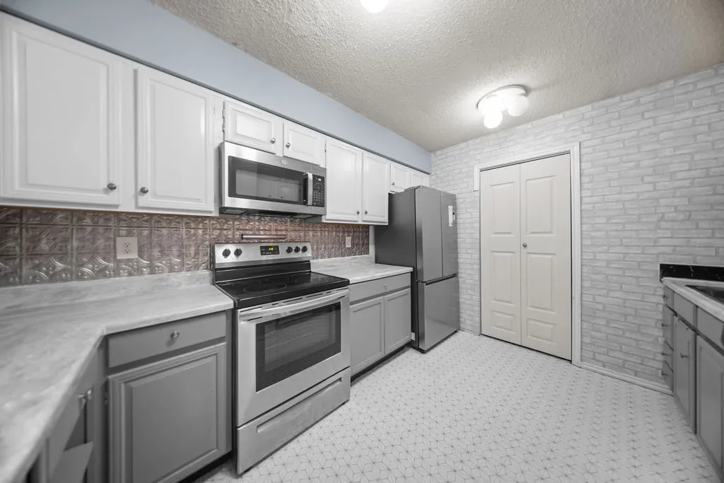 Kitchen featuring stainless steel appliances, upper white cabinetry, lower gray cabinetry, gray patterned countertops, and a textured backsplash
