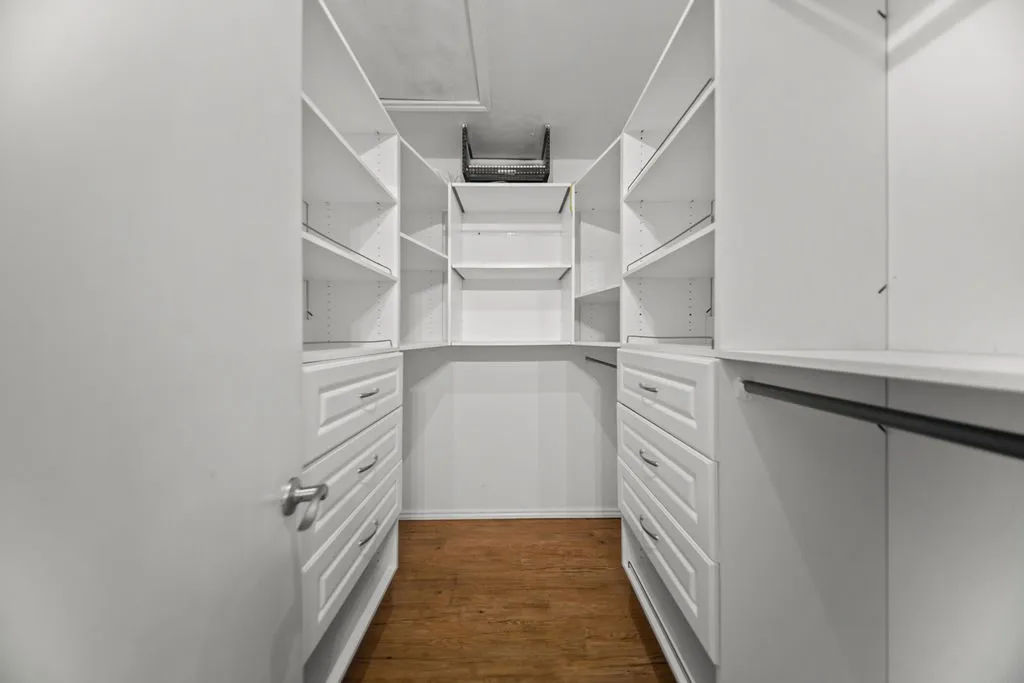 Custom closet system featuring white cabinetry and wood-finish flooring