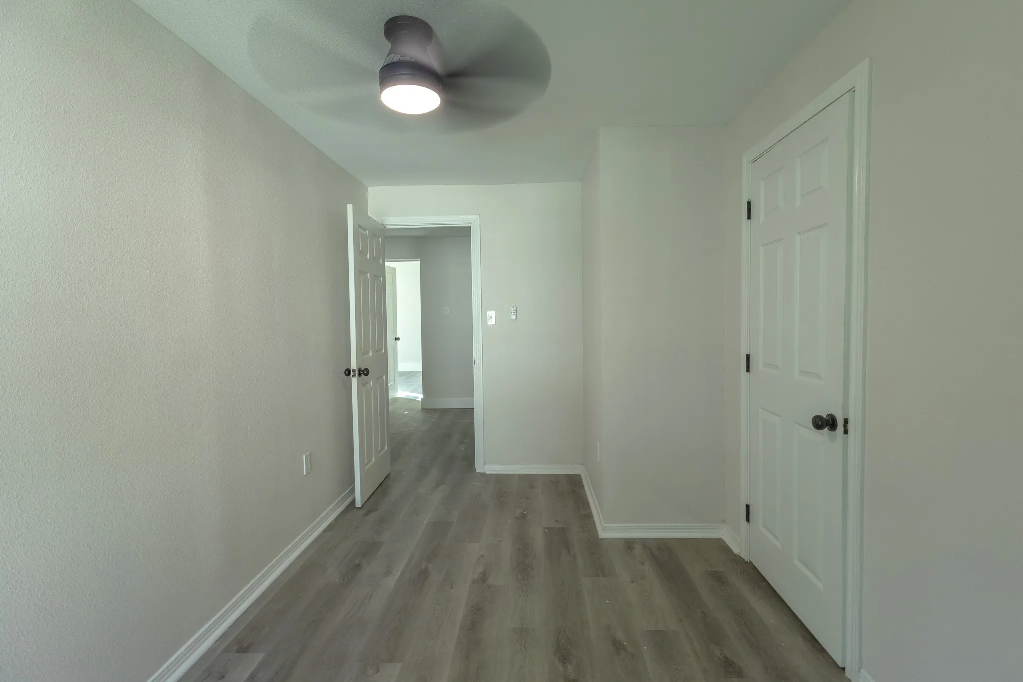 Neutral-toned room featuring a ceiling fan with integrated lighting, wood-finish flooring, and white trim