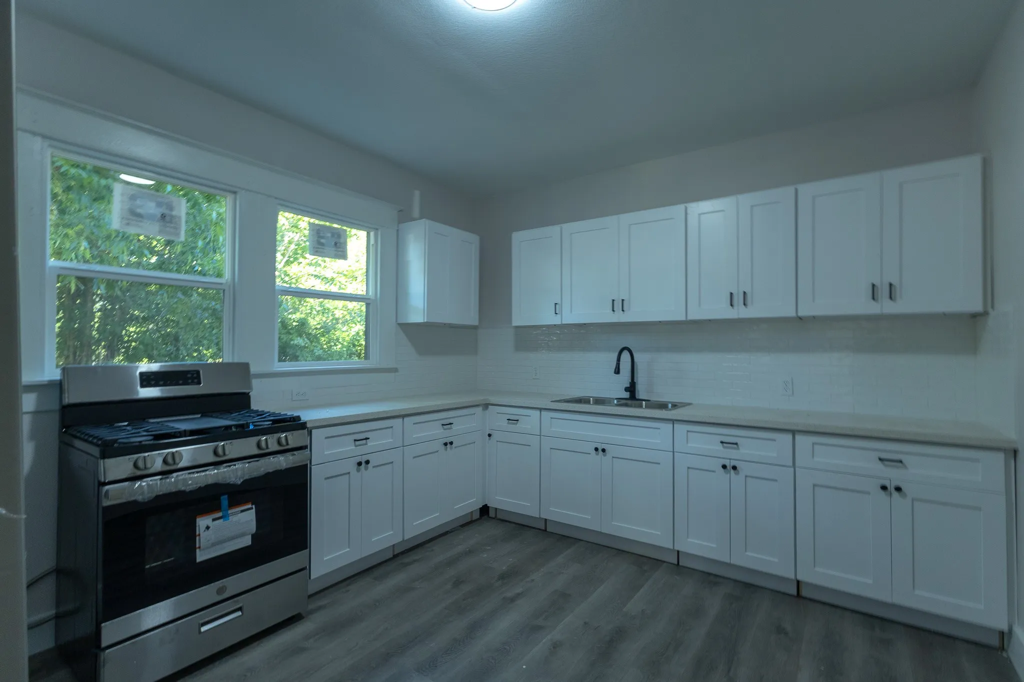Kitchen featuring white shaker cabinetry, stainless steel range, light-toned countertops, white subway tile backsplash, and wood-finish flooring