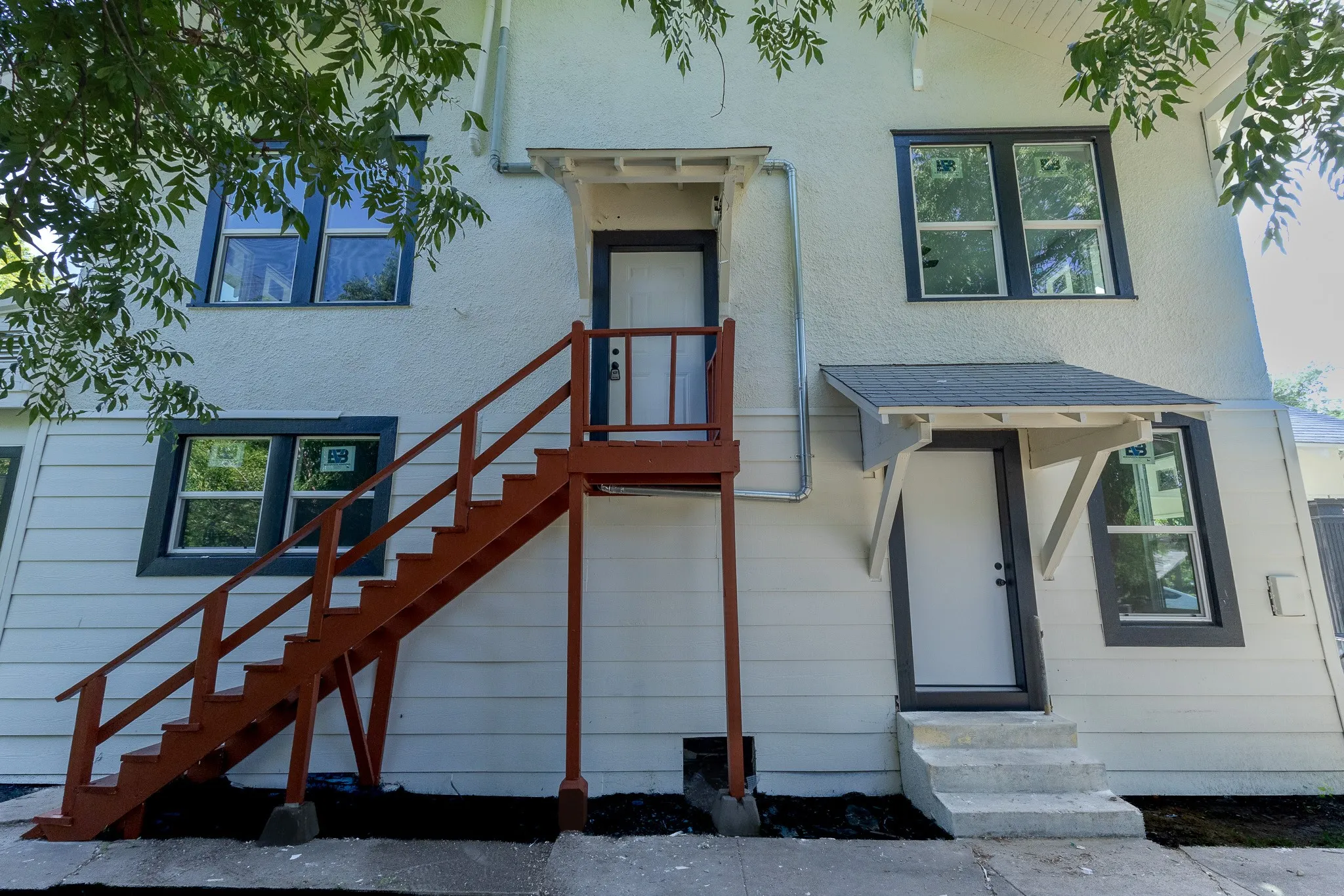 Exterior featuring white stucco and siding, dark-trimmed windows, a detached exterior staircase, a ground-level entry with steps and overhang, and an upper-level entry with an overhang