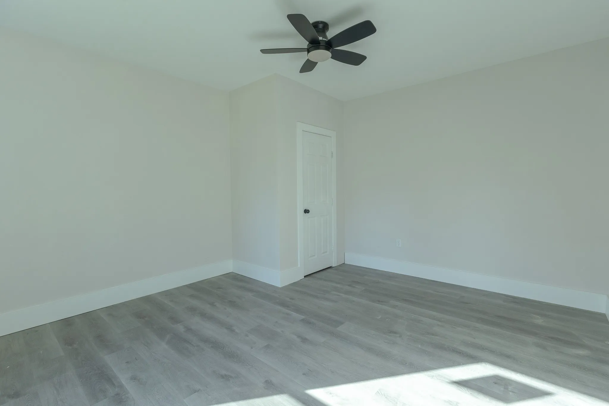 Spacious room featuring light gray walls, white baseboards, and a contemporary black ceiling fan