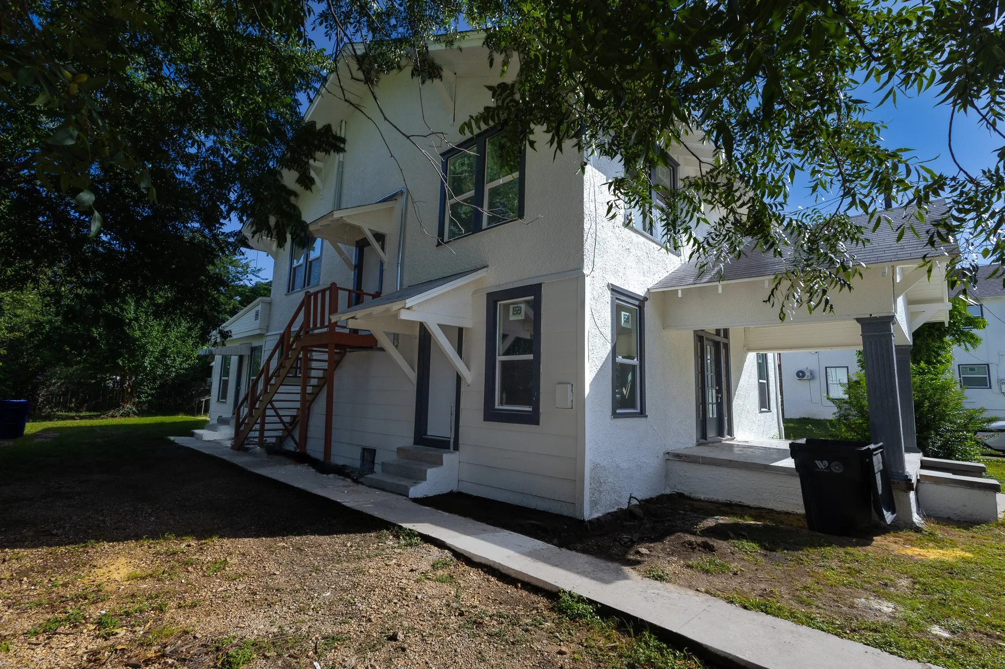 Stucco exterior with contrasting trim, featuring multiple windows, an exterior staircase, a covered porch, and a concrete walkway