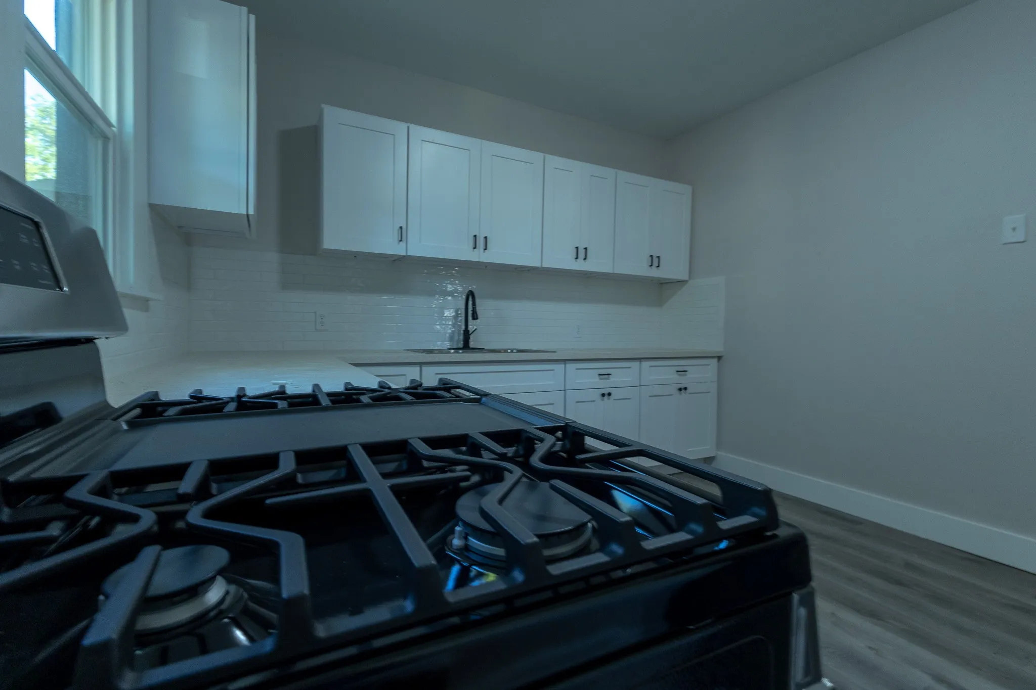 Stainless steel range with a gas cooktop, complemented by white shaker cabinetry, light-toned countertops, a white subway tile backsplash, and wood-finish flooring