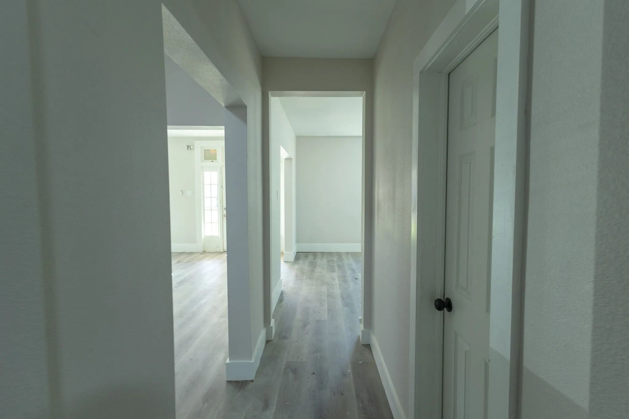 Interior hallway featuring light wood-finish flooring, neutral wall tones, white baseboards, and doorways leading to additional rooms